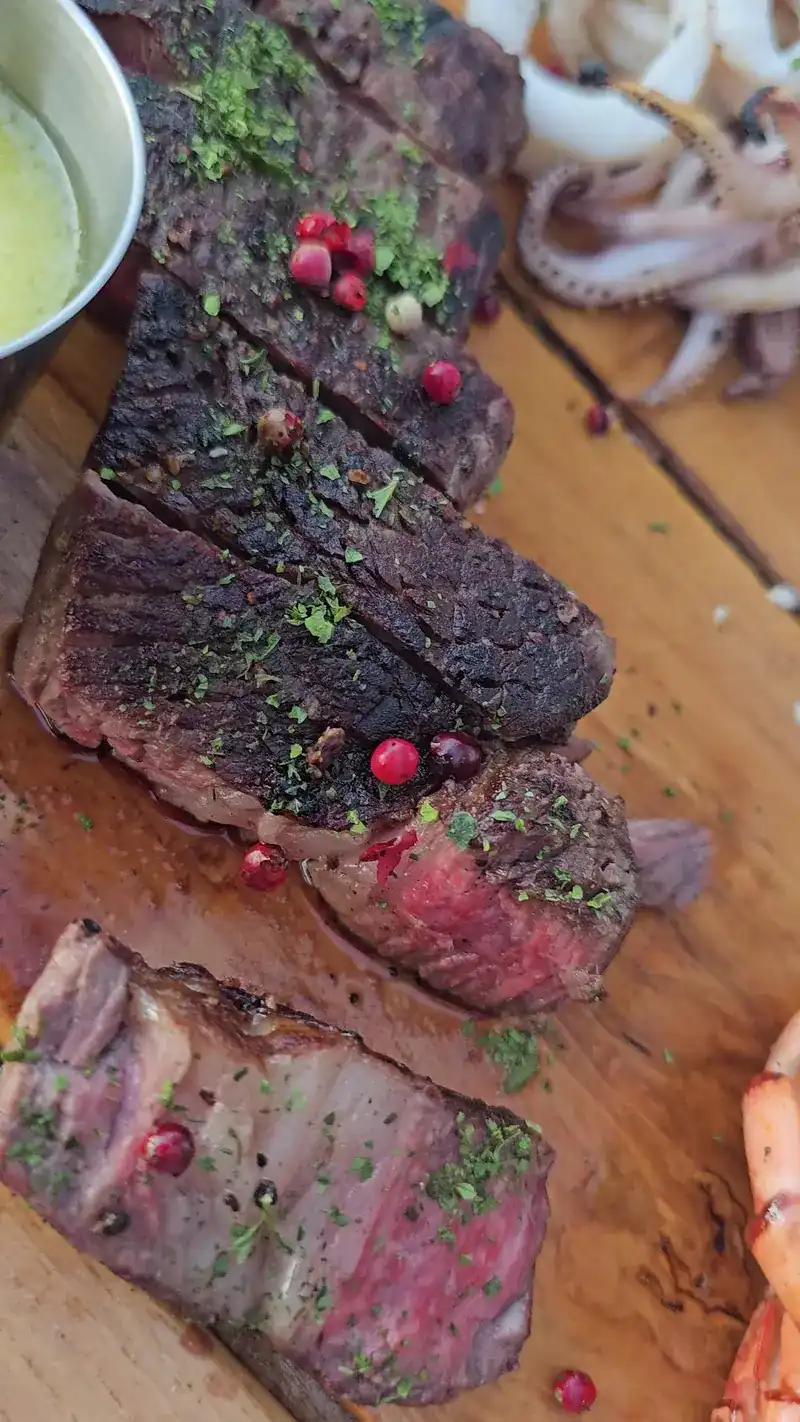 Sliced grilled steak with pink peppercorns on a wooden board