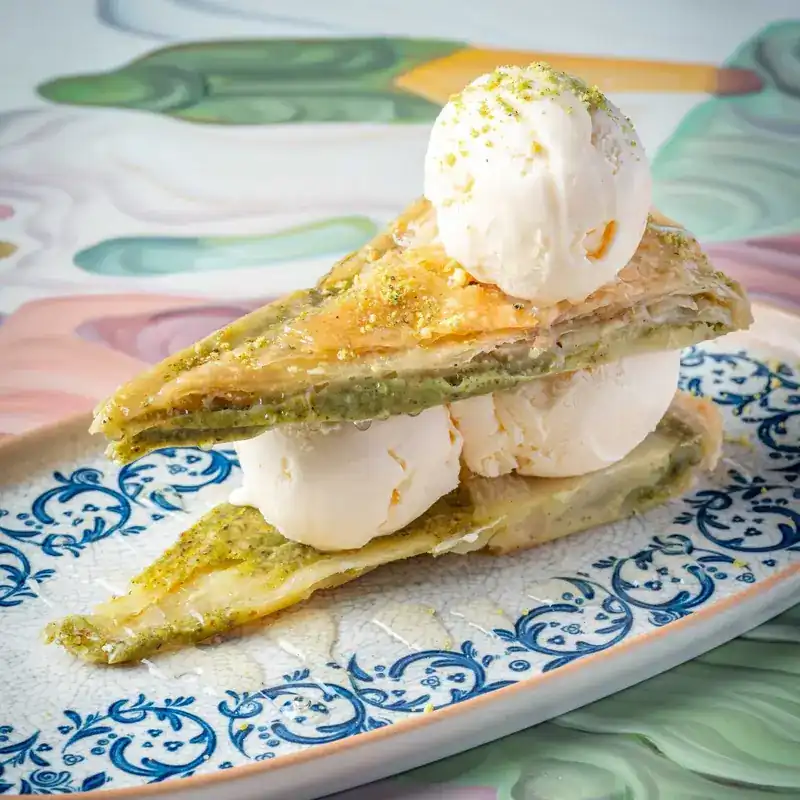 Layered pistachio pastry with scoops of ice cream on a blue patterned plate