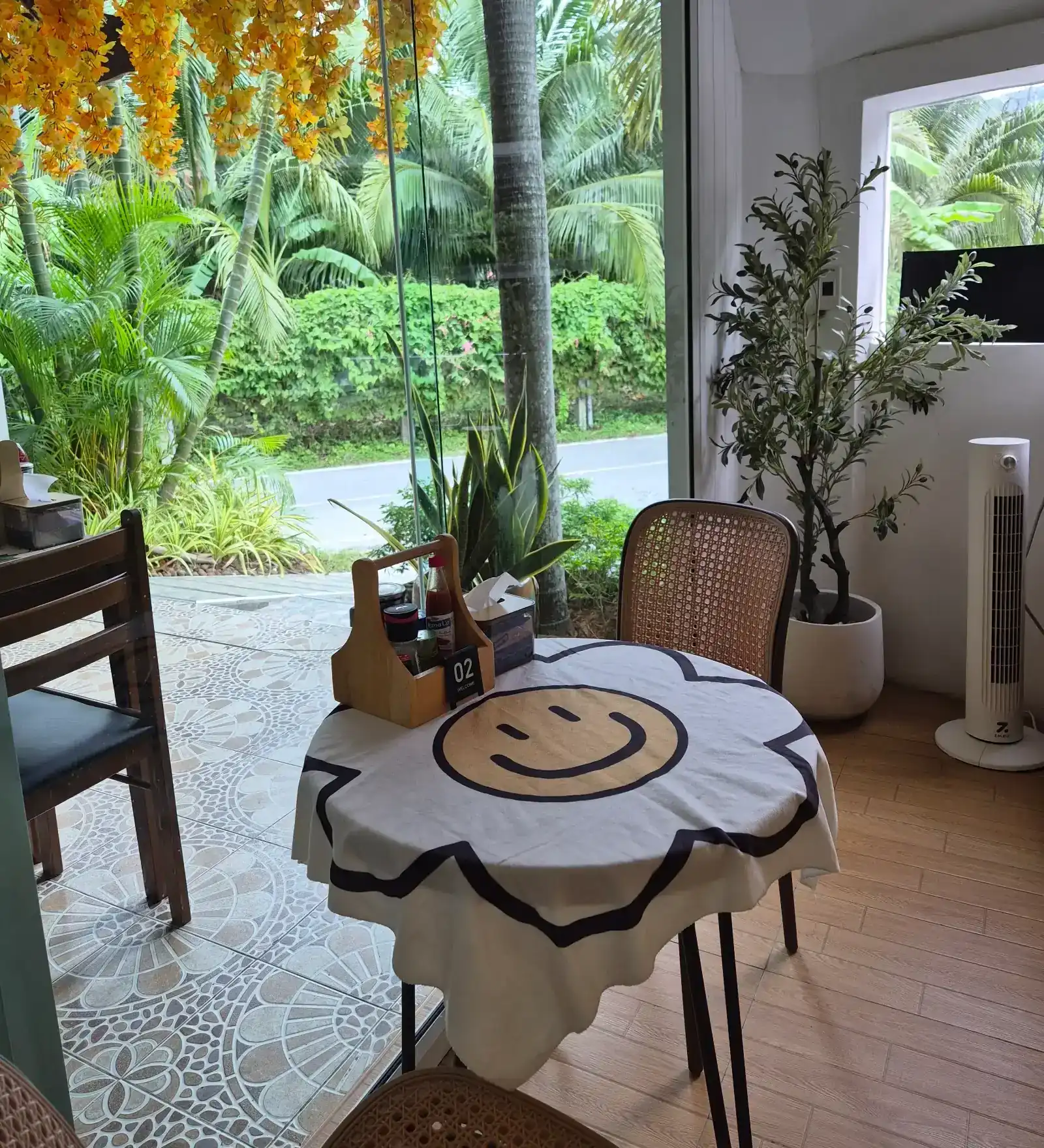 A table with a smiley tablecloth by the open glass front, palms outside