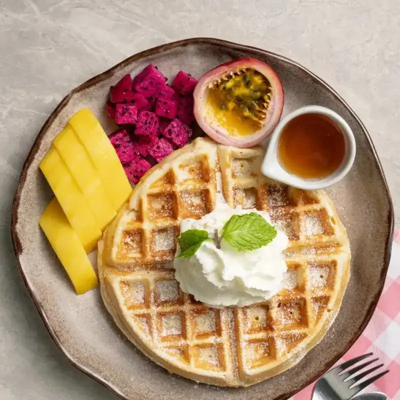 A waffle with cream, mango, dragon fruit and passion fruit