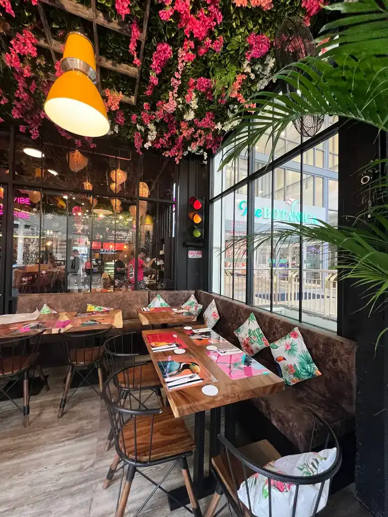 Corner banquette with tropical cushions under hanging flowers and a yellow lamp / มุมโซฟาพร้อมหมอนลายทรอปิคอลใต้ดอกไม้และโคมไฟสีเหลือง
