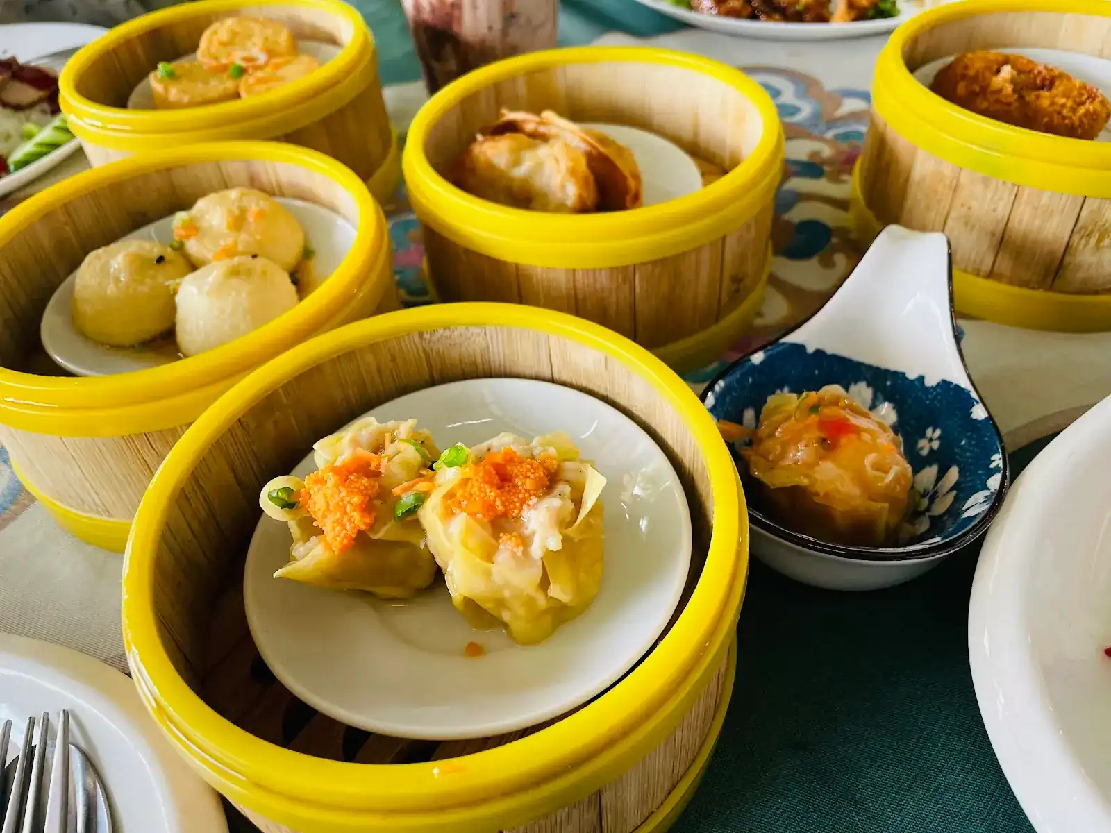 Several kinds of dim sum in yellow bamboo steamers on a patterned tablecloth