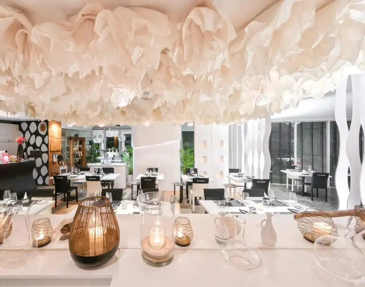 The white dining room under a ceiling of folded paper, tables set for dinner