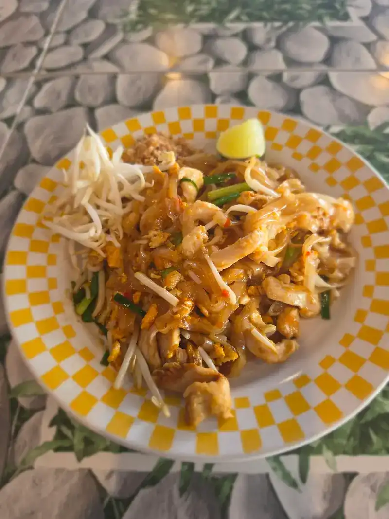 Pad thai with bean sprouts and a wedge of lime on a yellow chequered plate