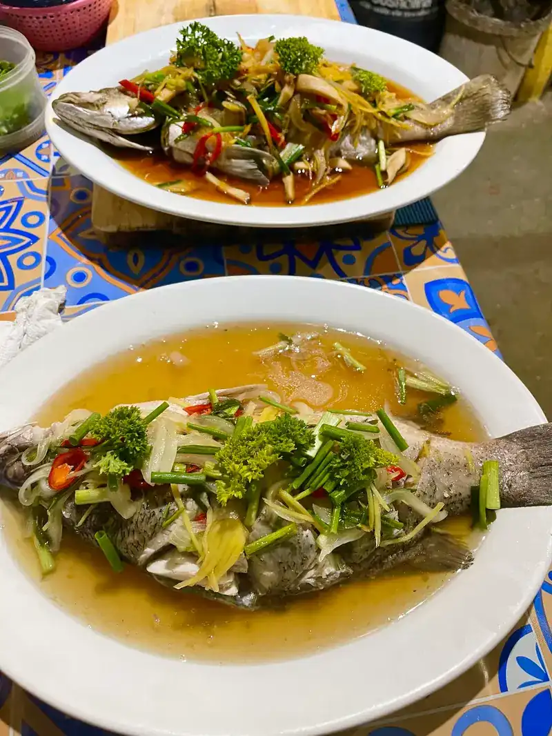 Two whole fish, one in a clear broth topped with herbs and chilli