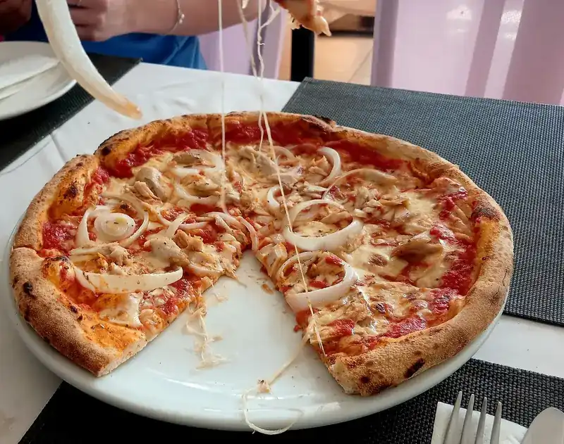 Pizza with onion rings, a slice lifted with the cheese still stretching / พิซซ่าหน้าหอมใหญ่ ยกชิ้นขึ้นมาชีสยังยืด