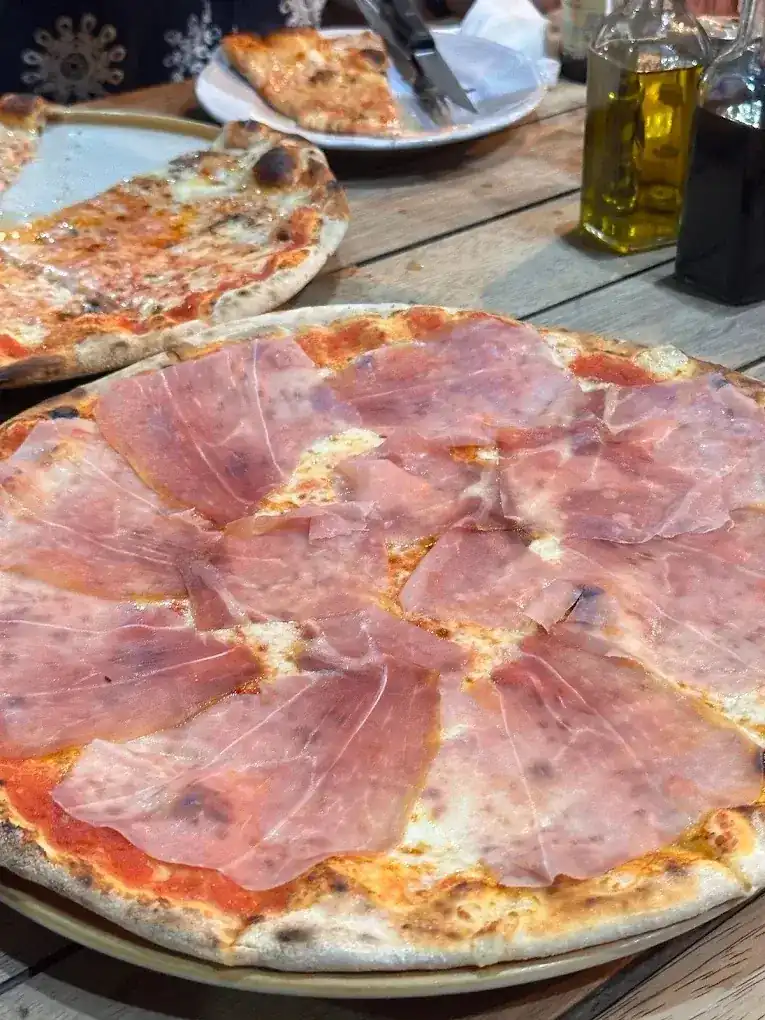 Wood-fired pizza covered with slices of Parma ham on a wooden table