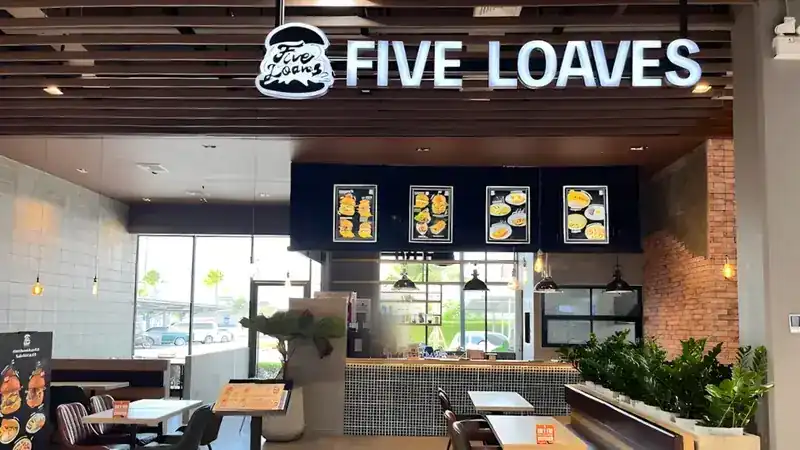 Inside: the counter under the Five Loaves sign, bench seating and plants