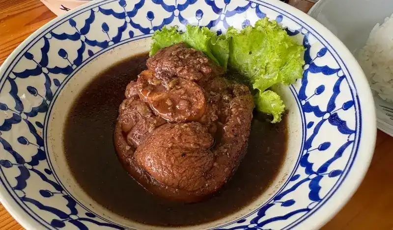 Braised pork in dark broth, in a blue-and-white bowl with lettuce