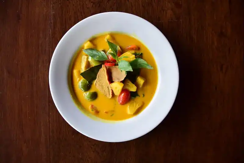 A curry with sliced roast duck, pineapple, cherry tomatoes and basil