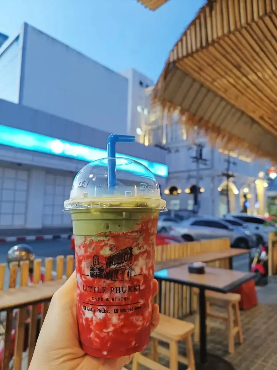 A matcha strawberry drink in a Little Phuket printed cup, held up at the roadside tables at dusk