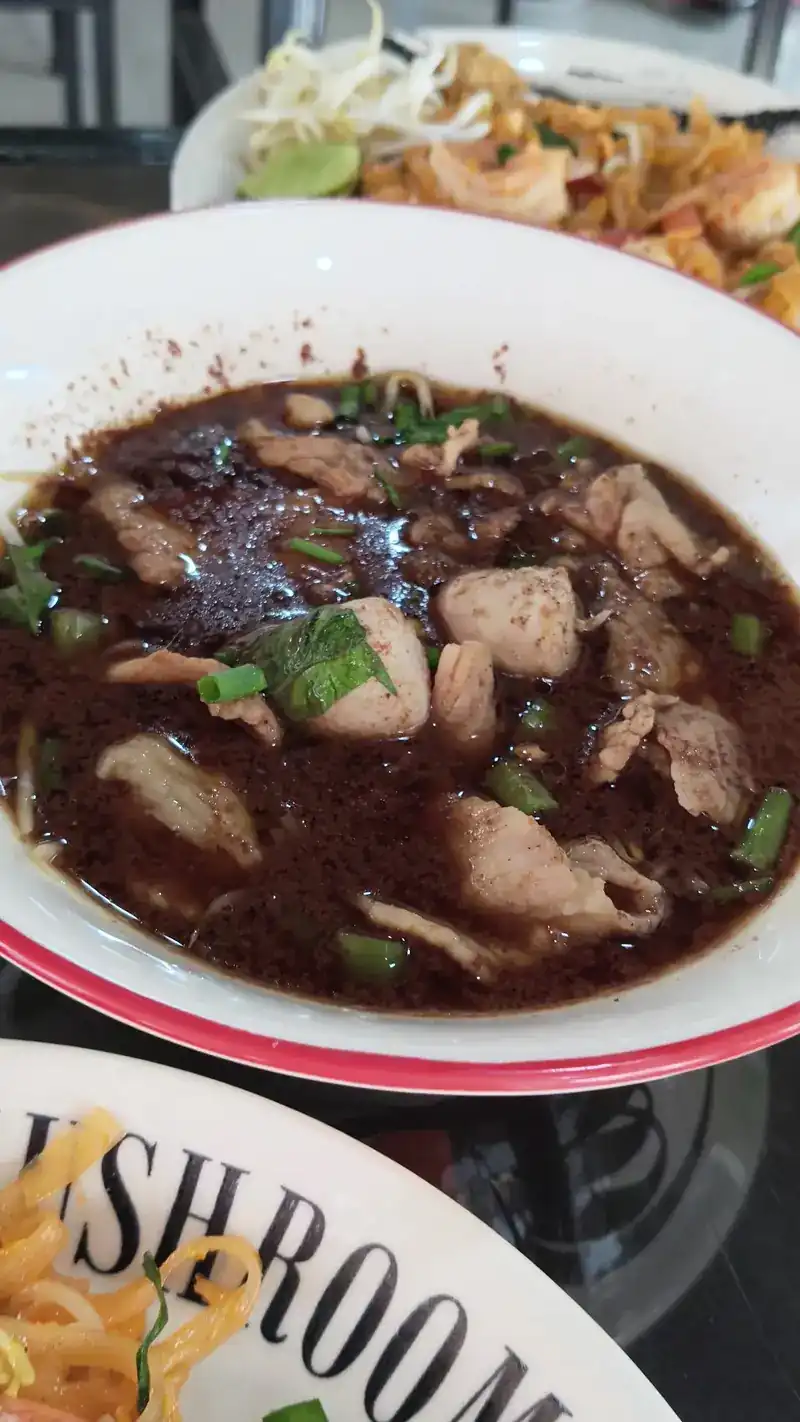 A bowl of boat noodles in dark broth with sliced pork, meatballs and spring onion