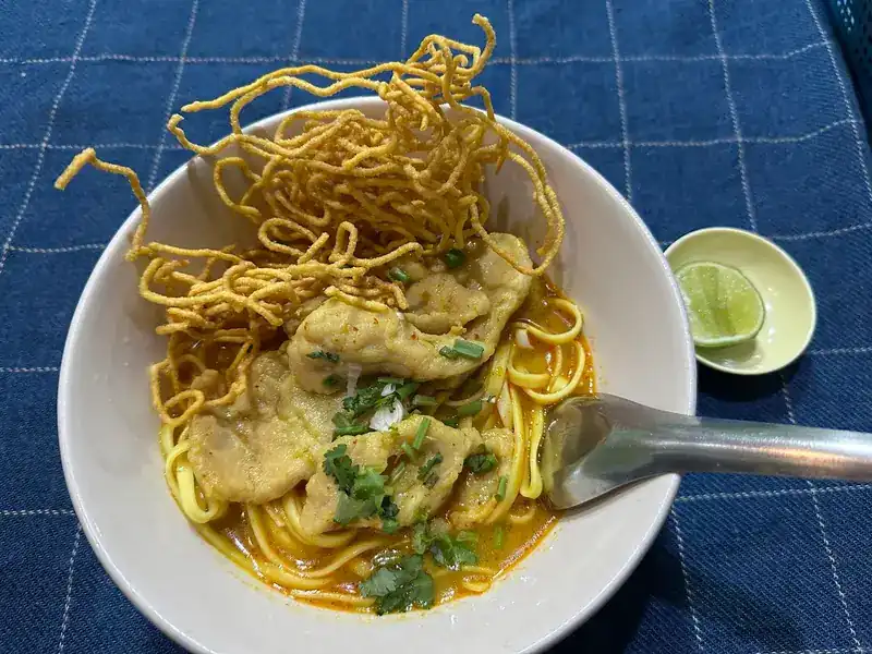 Khao soi with crispy noodles piled high and lime on the side, on an indigo cloth