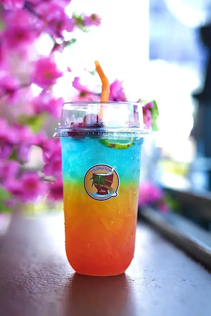 A layered blue-to-orange iced drink beside a branch of pink blossom