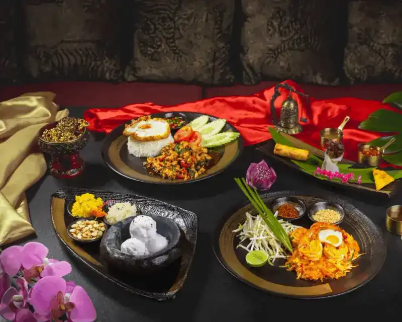 Thai dishes on dark plates: stir-fry with rice and a fried egg, Pad Thai with prawns, coconut ice cream in a stone bowl