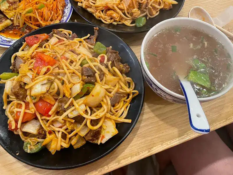 Stir-fried noodles with beef, tomato, peppers and cabbage, with a bowl of soup