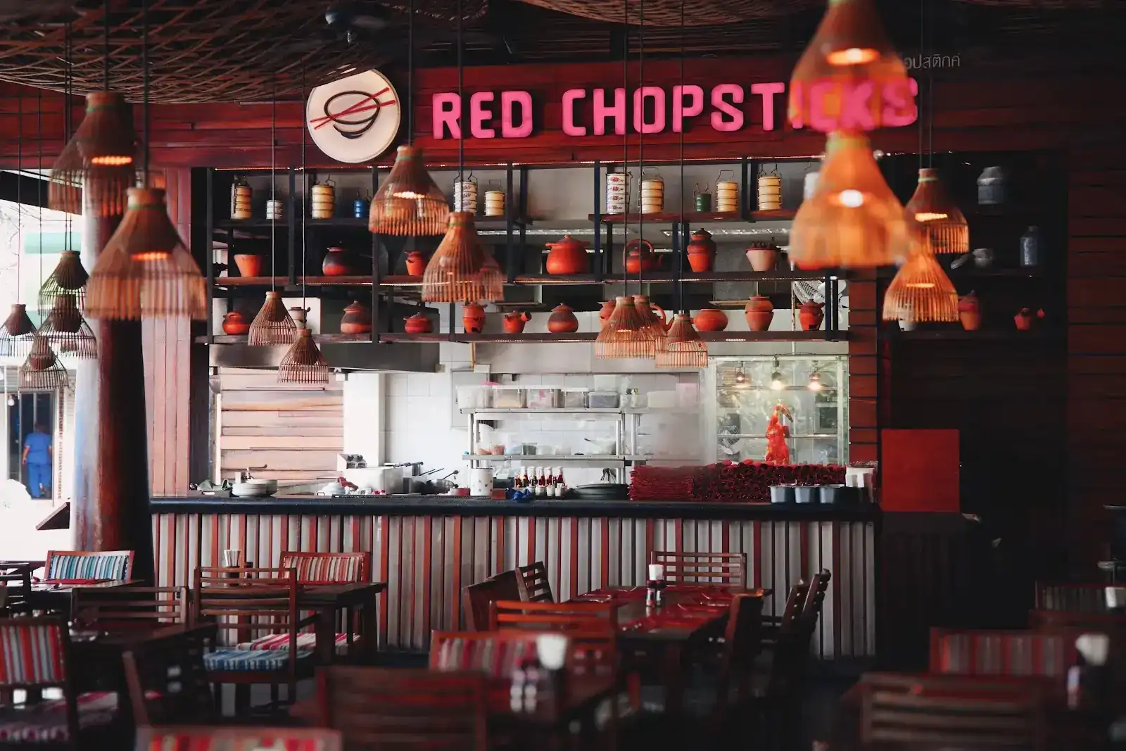 The open kitchen under the pink neon Red Chopsticks sign, with bamboo lanterns and shelves of clay pots
