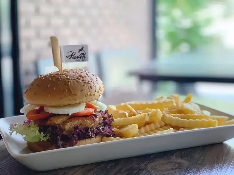 A burger with crinkle-cut fries, a small Surin Chill House flag on top