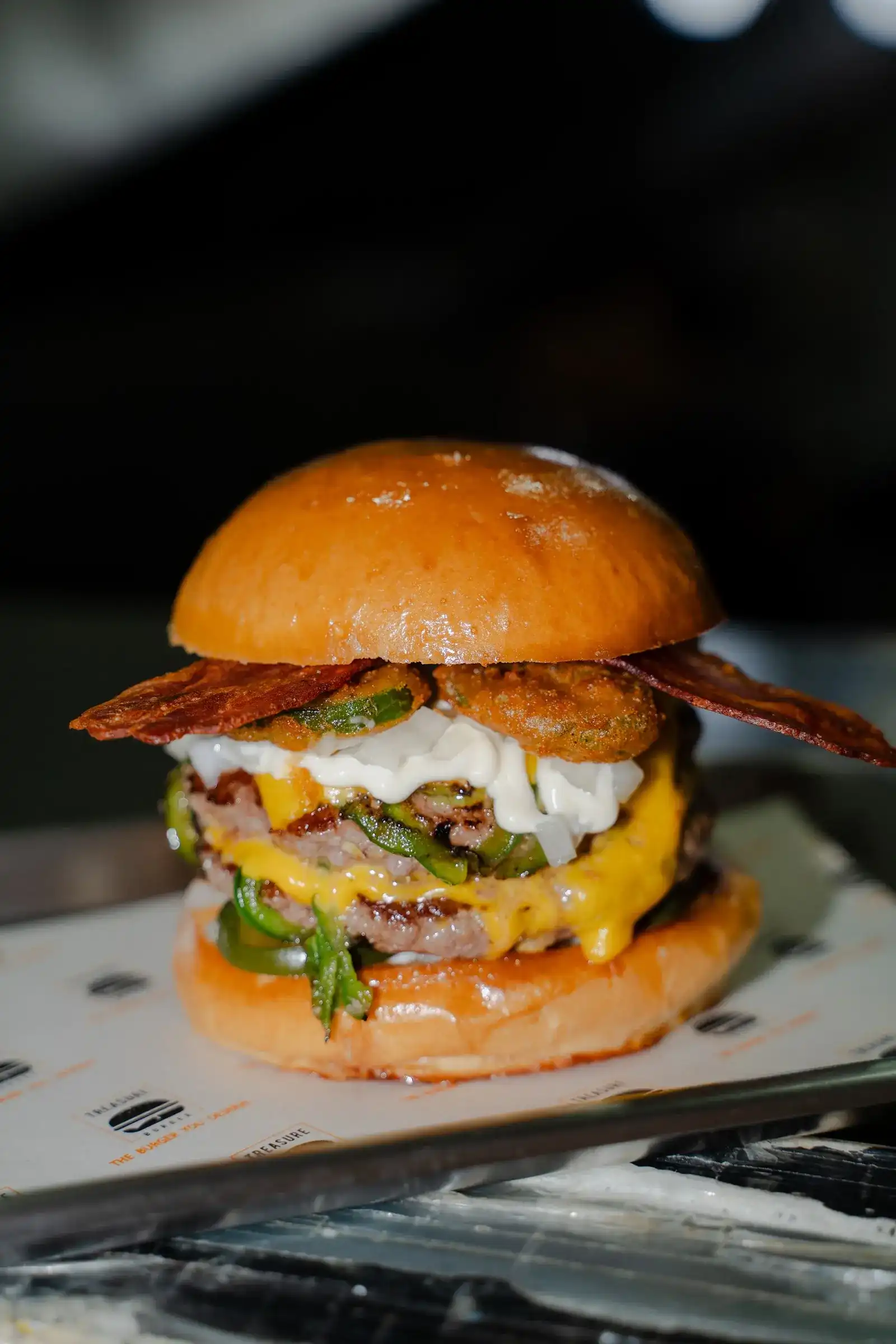 Burger with bacon, fried jalapeños, white sauce, cheddar and beef on a homemade bun / เบอร์เกอร์เบคอน ฮาลาเปโนทอด ซอสขาว ชีสเชดดาร์ และเนื้อ ในขนมปังทำเอง