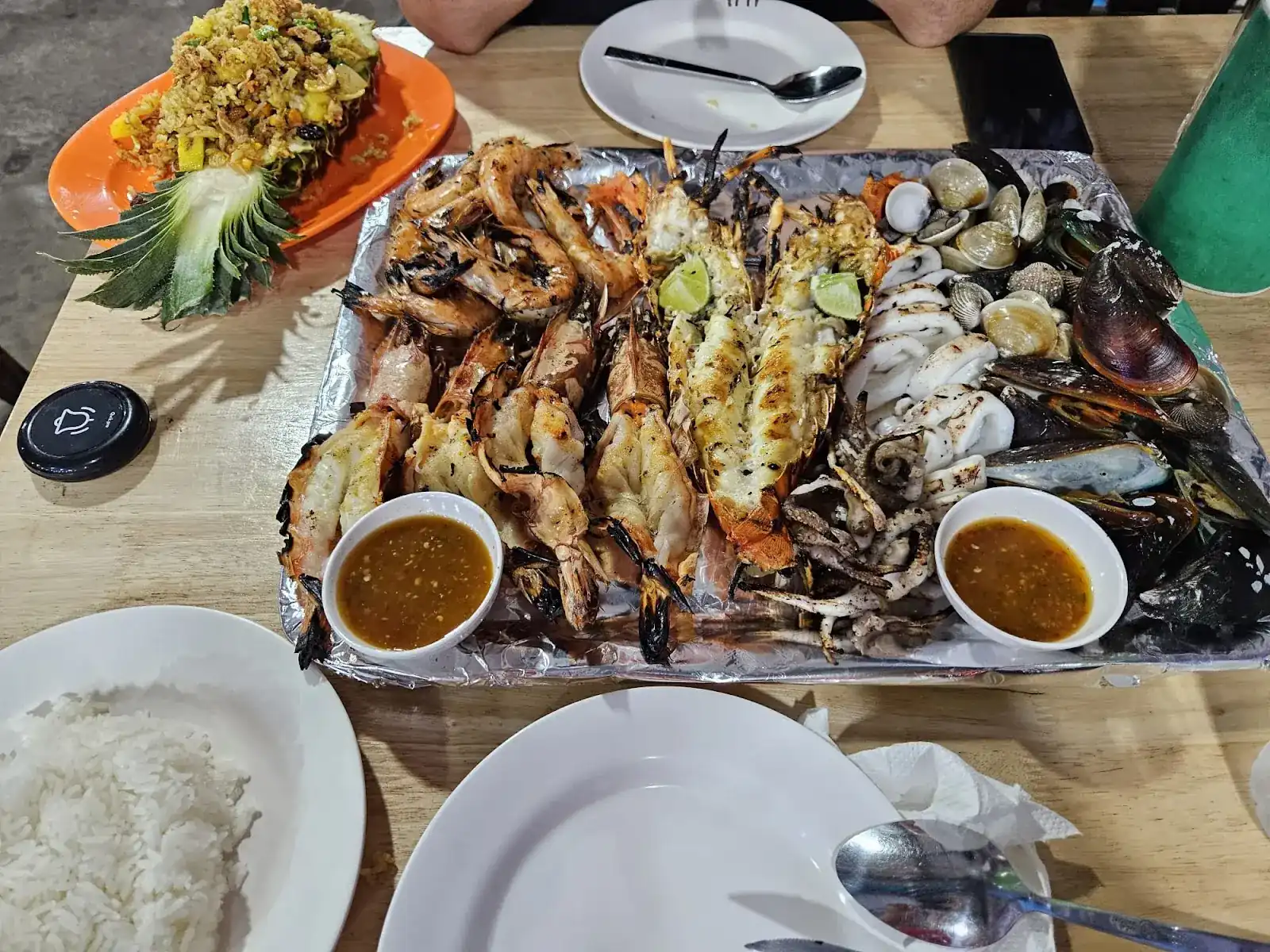 A tray of grilled prawns, lobster, squid, clams and mussels with two dipping sauces, rice and pineapple fried rice