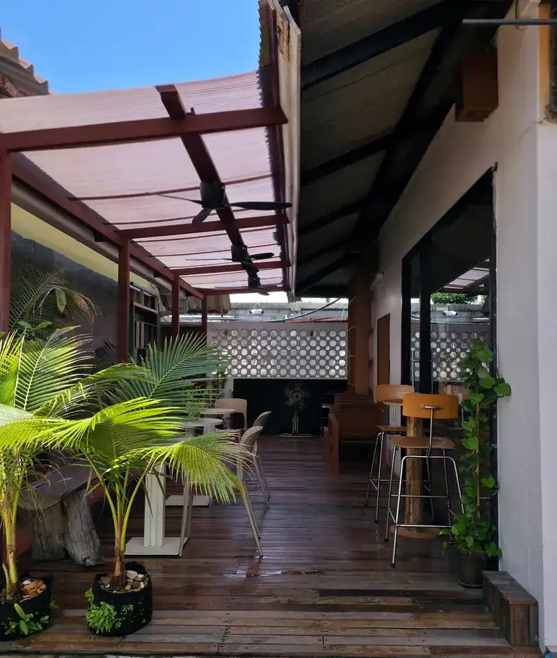 The terrace: a wooden deck under a pergola, with palms and bar stools along the wall