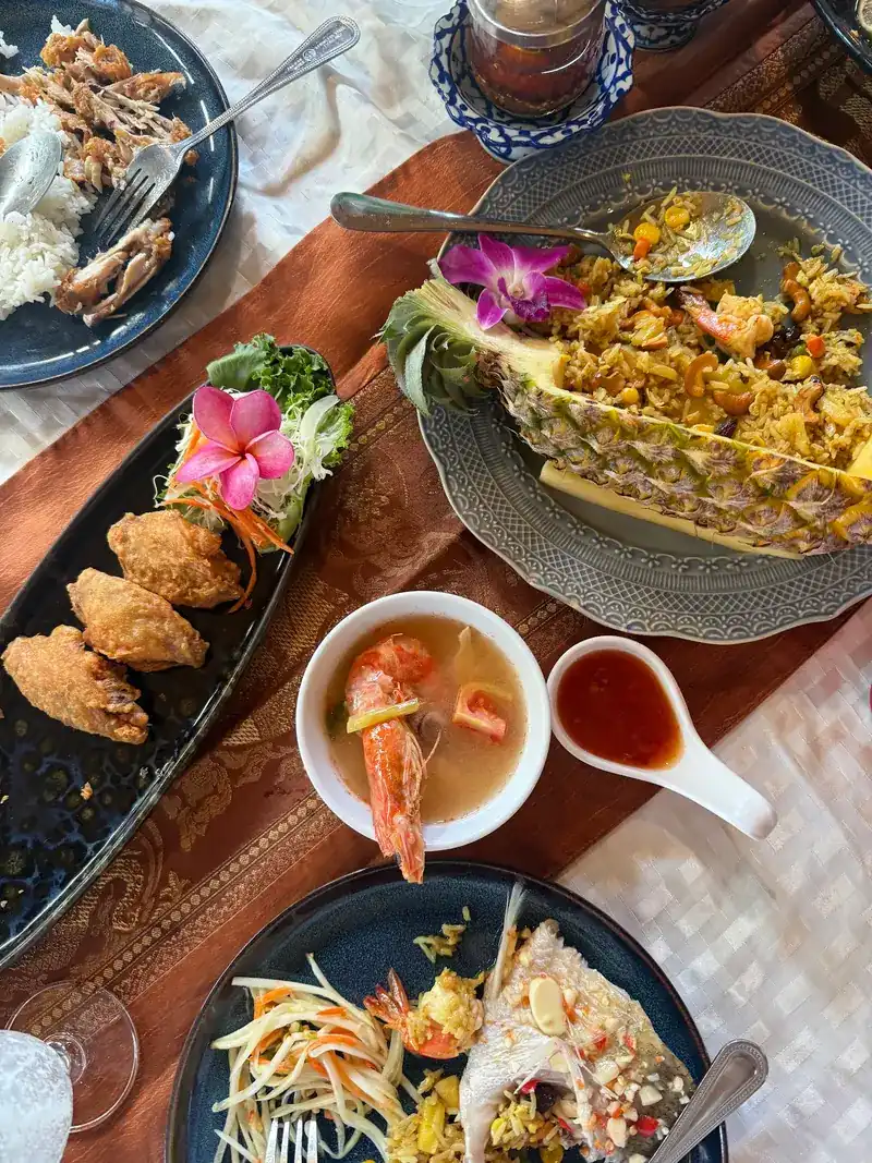 Seen from above: pineapple fried rice in a pineapple half, golden fried pieces, a small bowl of prawn soup and a papaya salad