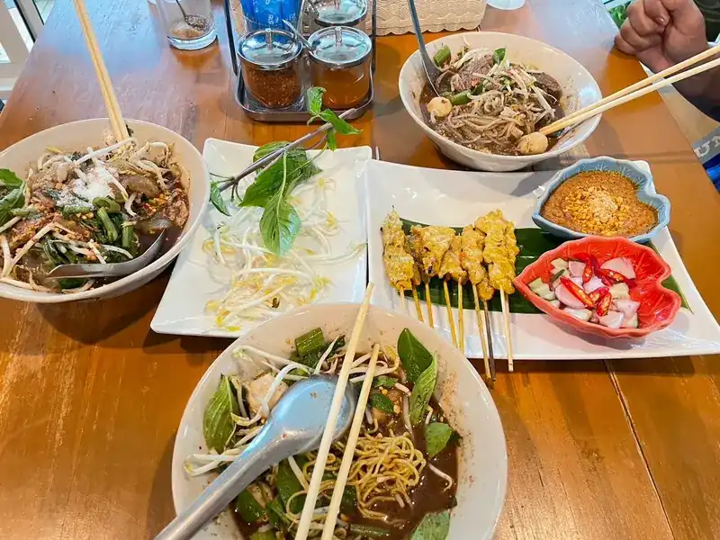 A table of boat noodles, pork satay, bean sprouts and fresh basil