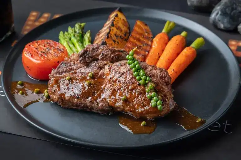 Steak with green peppercorn sauce, grilled tomato, asparagus and baby carrots