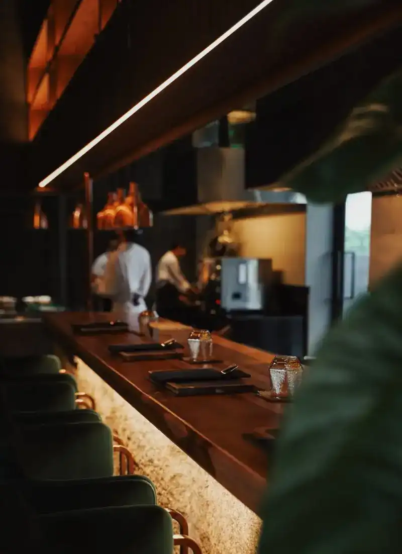 The wooden sushi counter with green velvet stools and the open kitchen beyond
