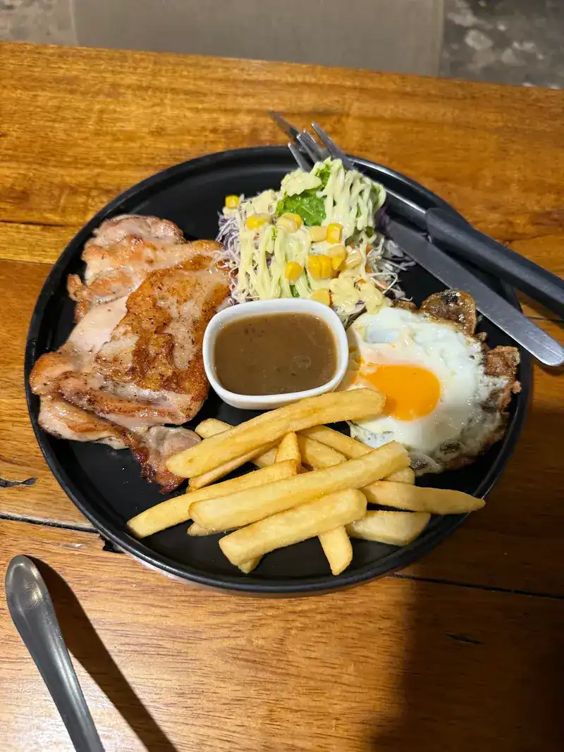 Chicken steak with fries, a fried egg, salad and a cup of sauce on a black plate / สเต๊กไก่กับเฟรนช์ฟรายส์ ไข่ดาว สลัด และน้ำซอสถ้วยเล็กบนจานสีดำ