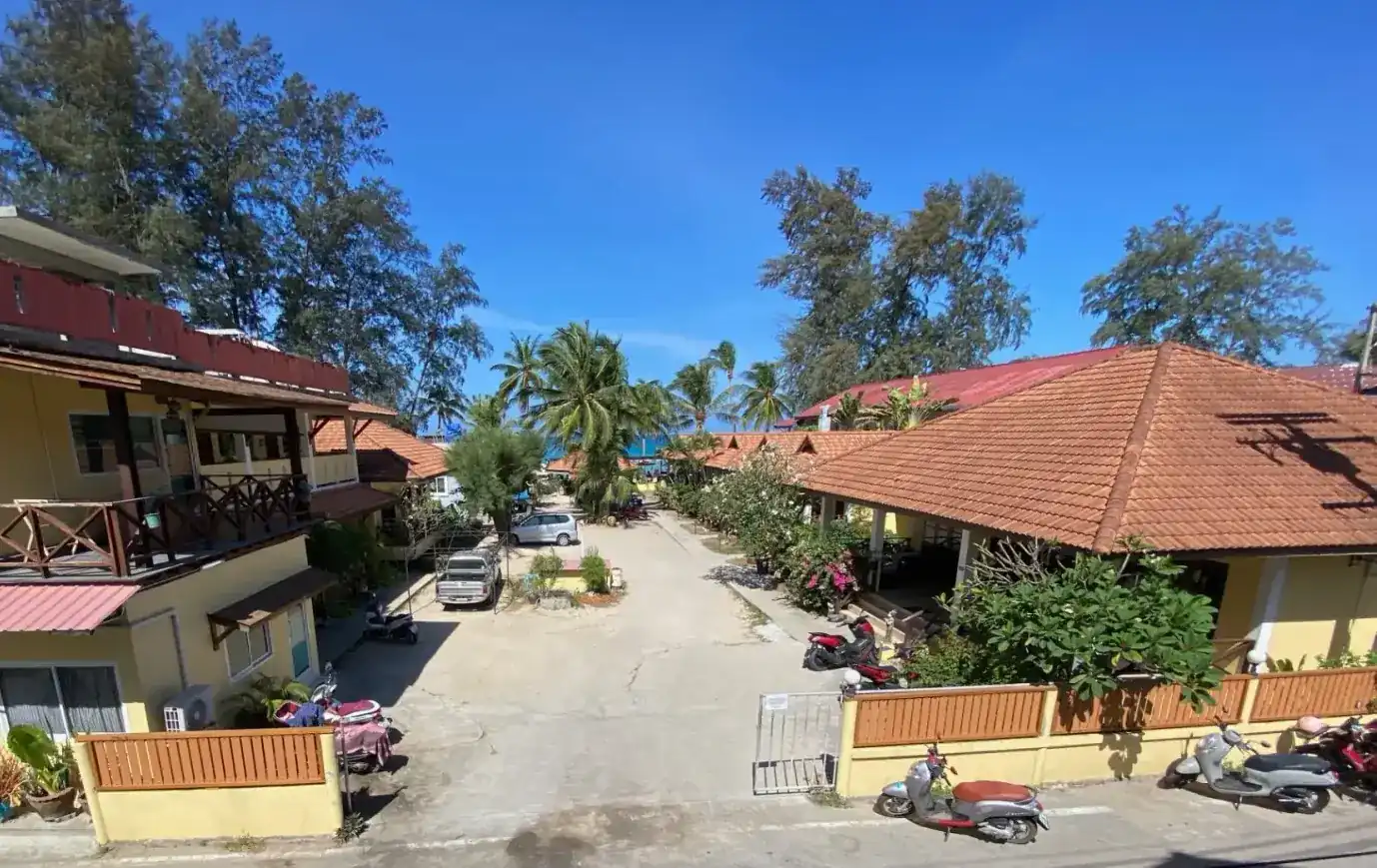 The lane through Coconut Garden, yellow houses with tiled roofs on both sides, palms and the sea at the far end