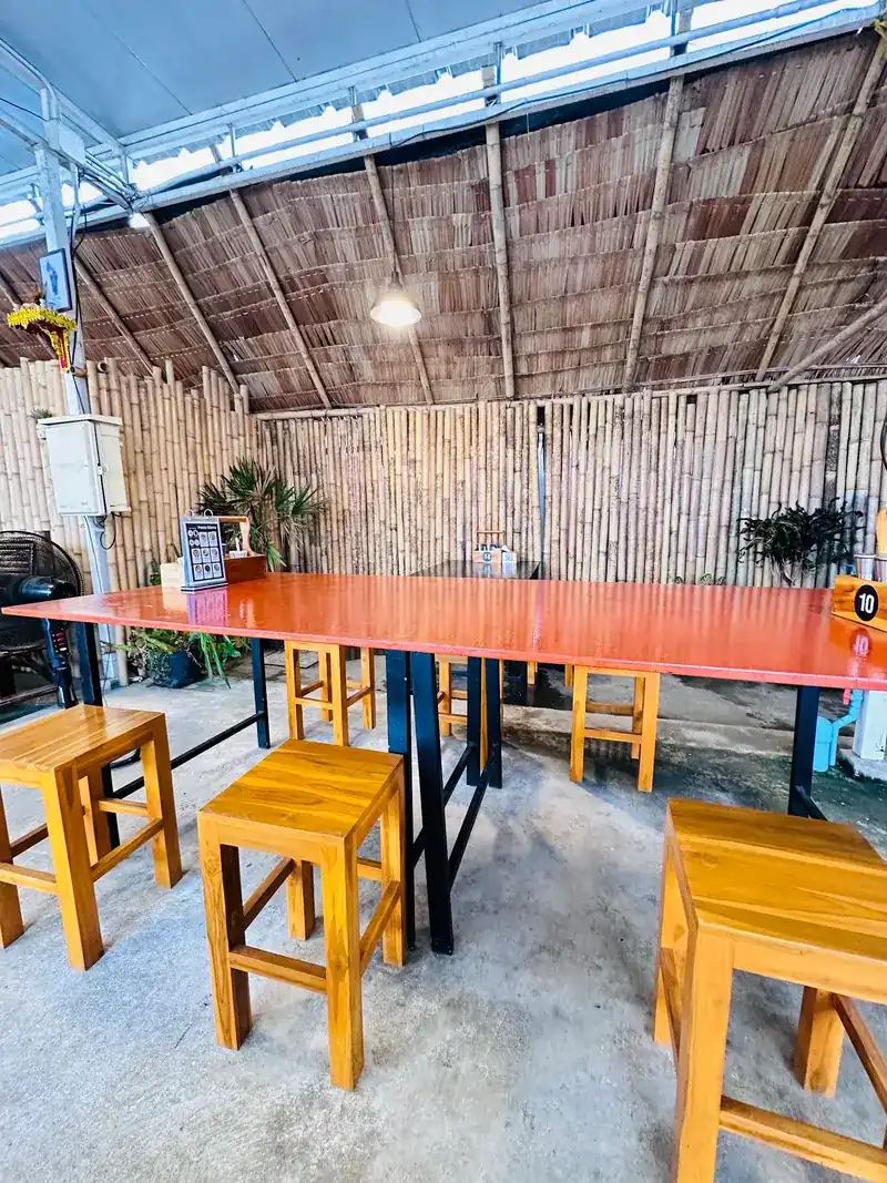 Long orange table and wooden stools against a bamboo wall