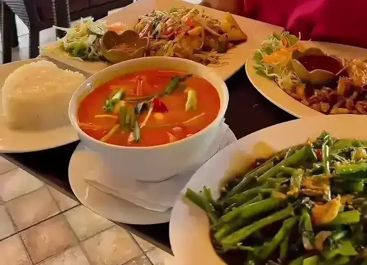 An orange Thai soup, rice, salads and stir-fried greens on a table.