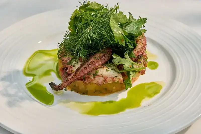 Grilled octopus under a pile of fresh herbs
