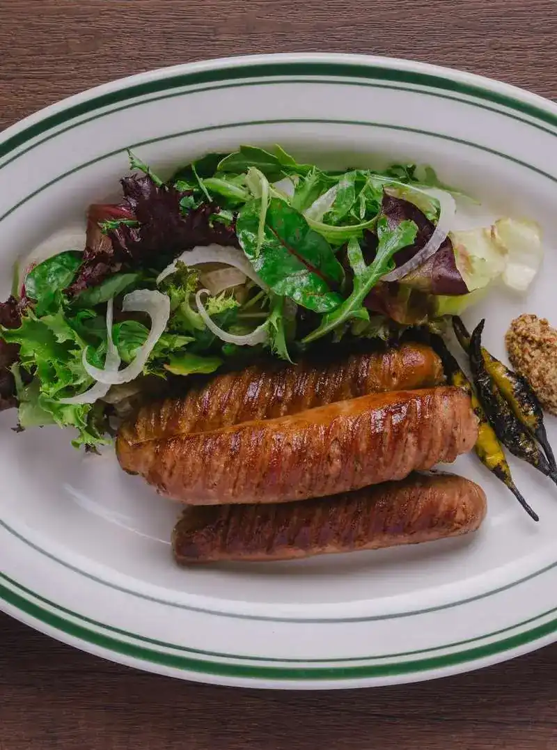 Grilled sausages with salad leaves and mustard on a green-rimmed plate