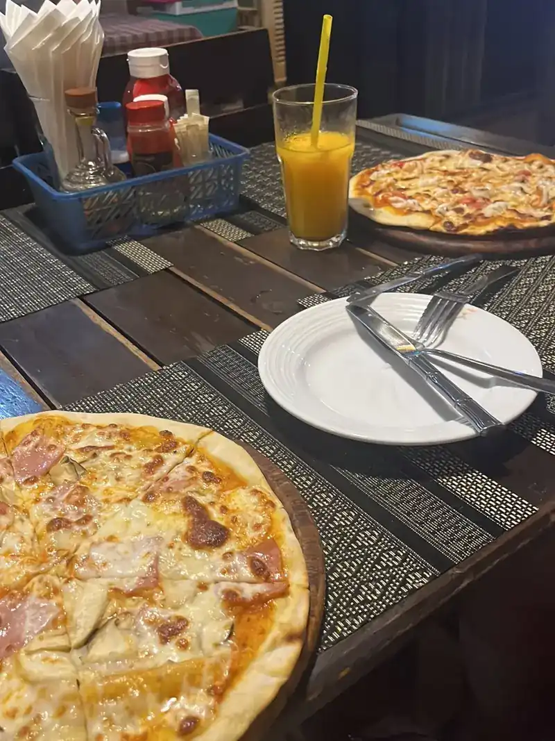 Two pizzas on wooden boards and a glass of juice on a dark wooden table