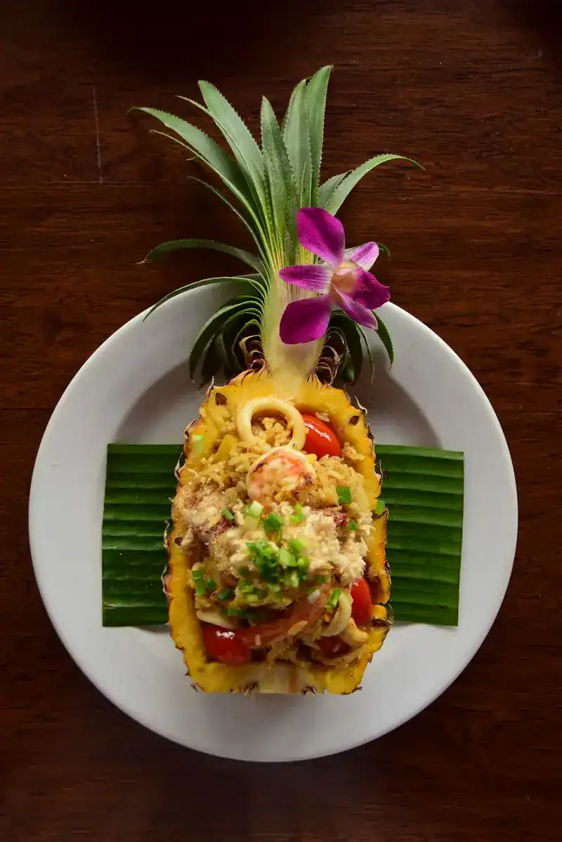 Pineapple fried rice with prawns and squid served in a pineapple half, topped with an orchid