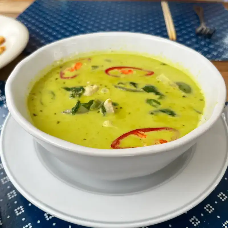 Green curry in a white bowl with sliced red chilli