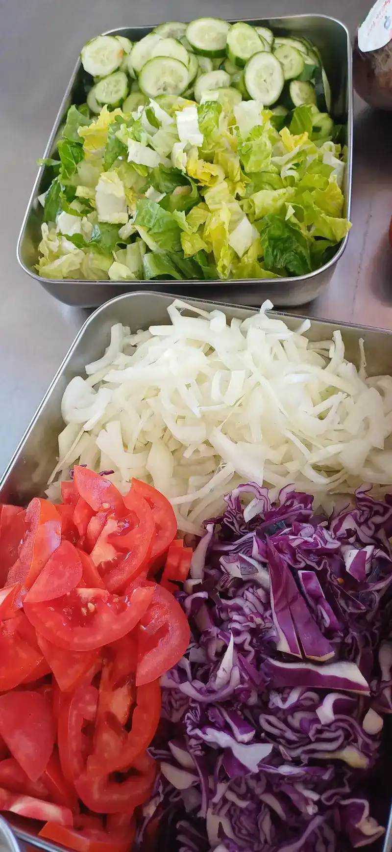 Steel trays of sliced cucumber, lettuce, tomato and red cabbage, cut and ready