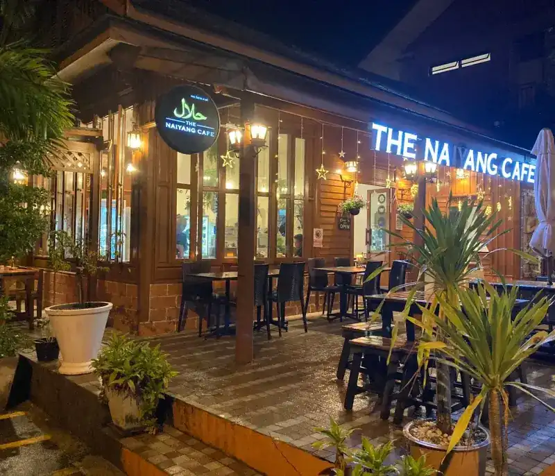 The cafe at night: its lit sign over the terrace, outdoor tables and potted palms