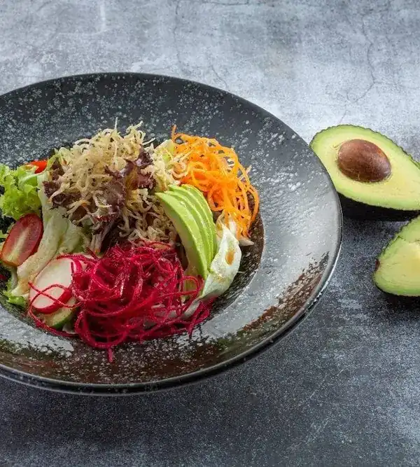 A salad of avocado, beetroot, carrot and crisp noodles in a dark bowl