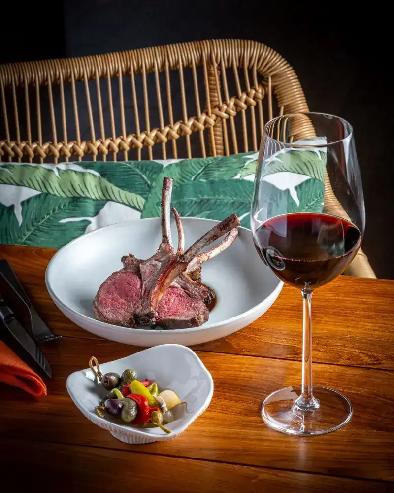 Lamb rack on a white plate beside a glass of red wine