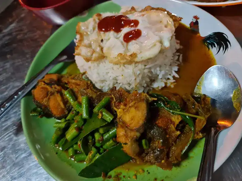 A spicy stir-fry with long beans next to rice with a fried egg, on a rooster plate