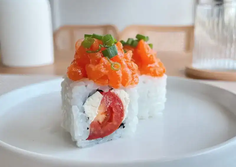 Two pieces of roll with cherry tomato and cream cheese, topped with chopped salmon and spring onion, on a white plate