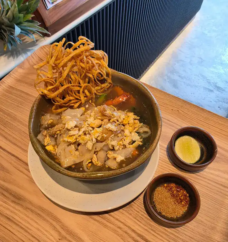 Noodle bowl topped with crispy noodles, lime and chili on the side