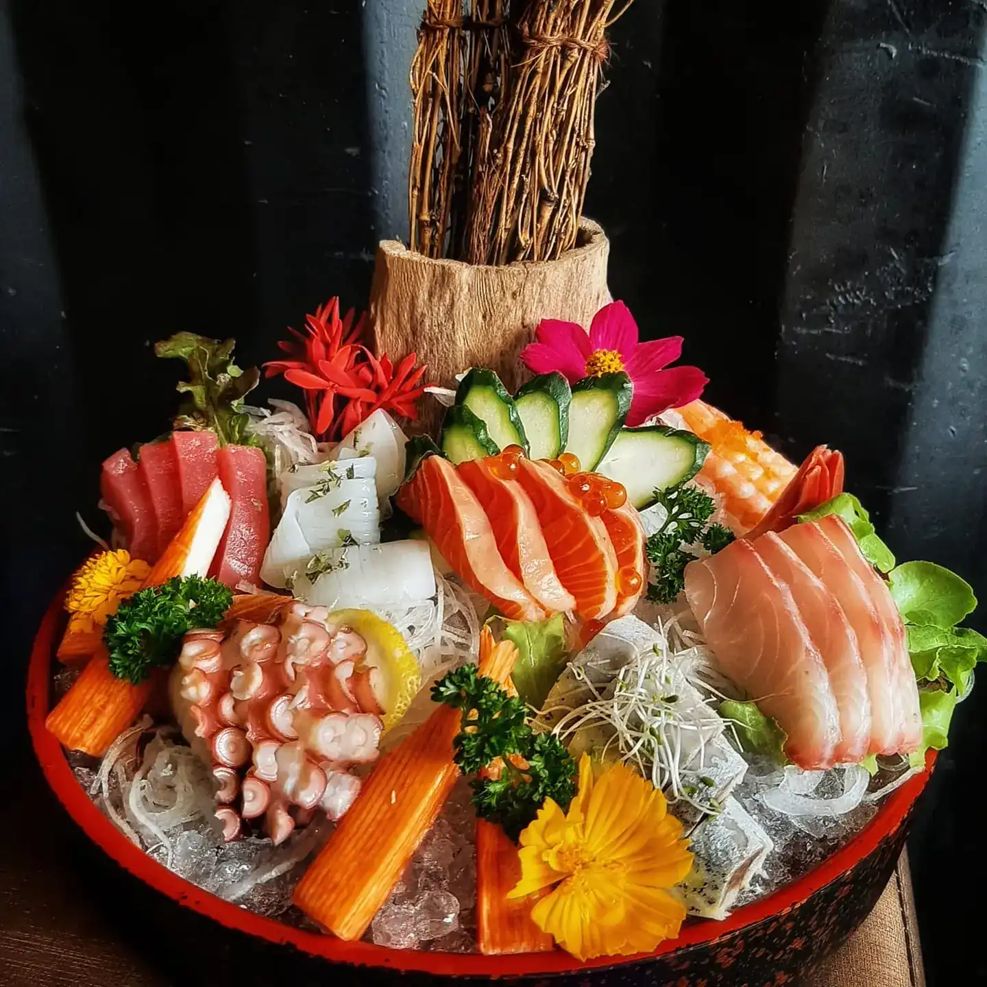 Sashimi on crushed ice in a red bowl: salmon with salmon roe, tuna, octopus, squid, white fish and crab sticks, decorated with flowers