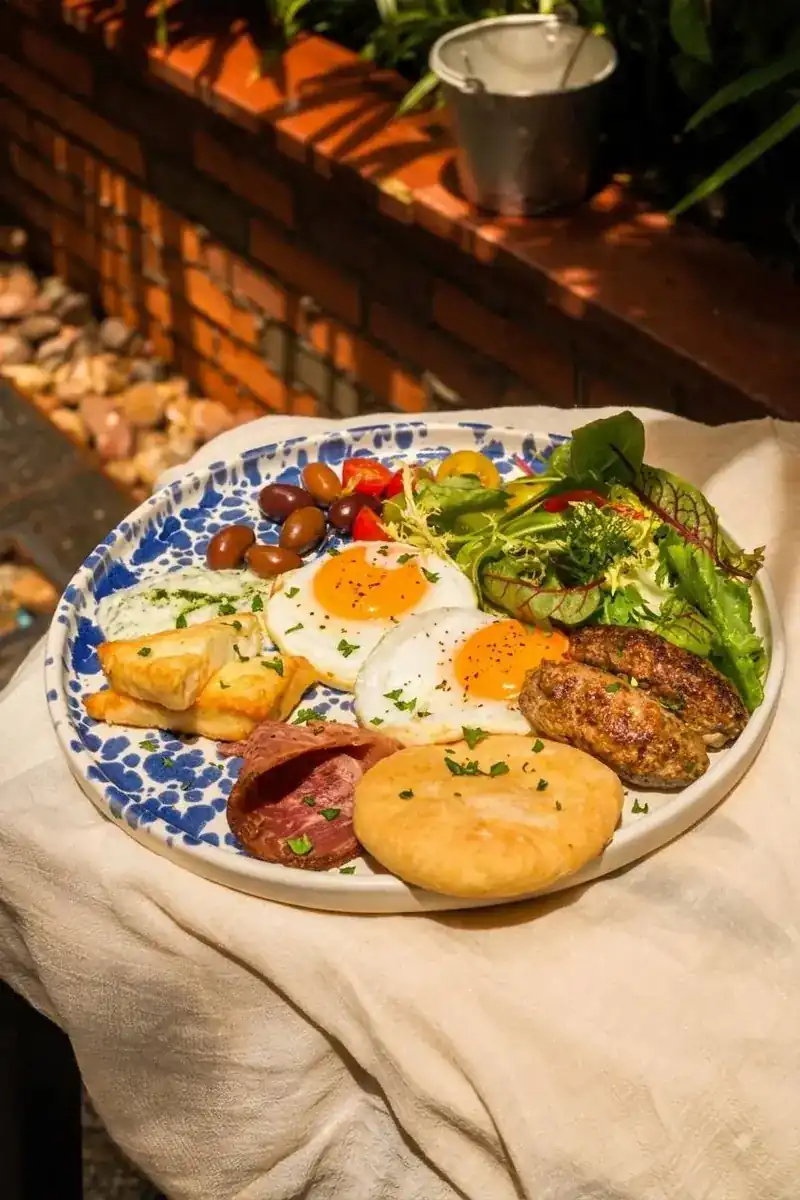A breakfast plate with fried eggs, meat patties, cured meat, flatbread and salad on a blue-patterned plate