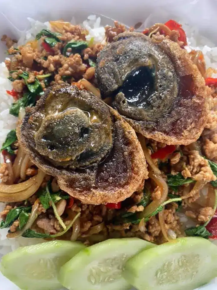 Holy basil stir-fry over rice with two crispy fried century eggs and cucumber slices — ผัดกะเพราราดข้าว ไข่เยี่ยวม้าทอดกรอบ กับแตงกวาหั่นแว่น