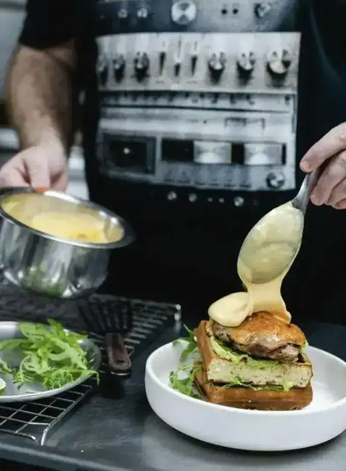 Hollandaise spooned over a stacked sandwich in the Melbourne kitchen