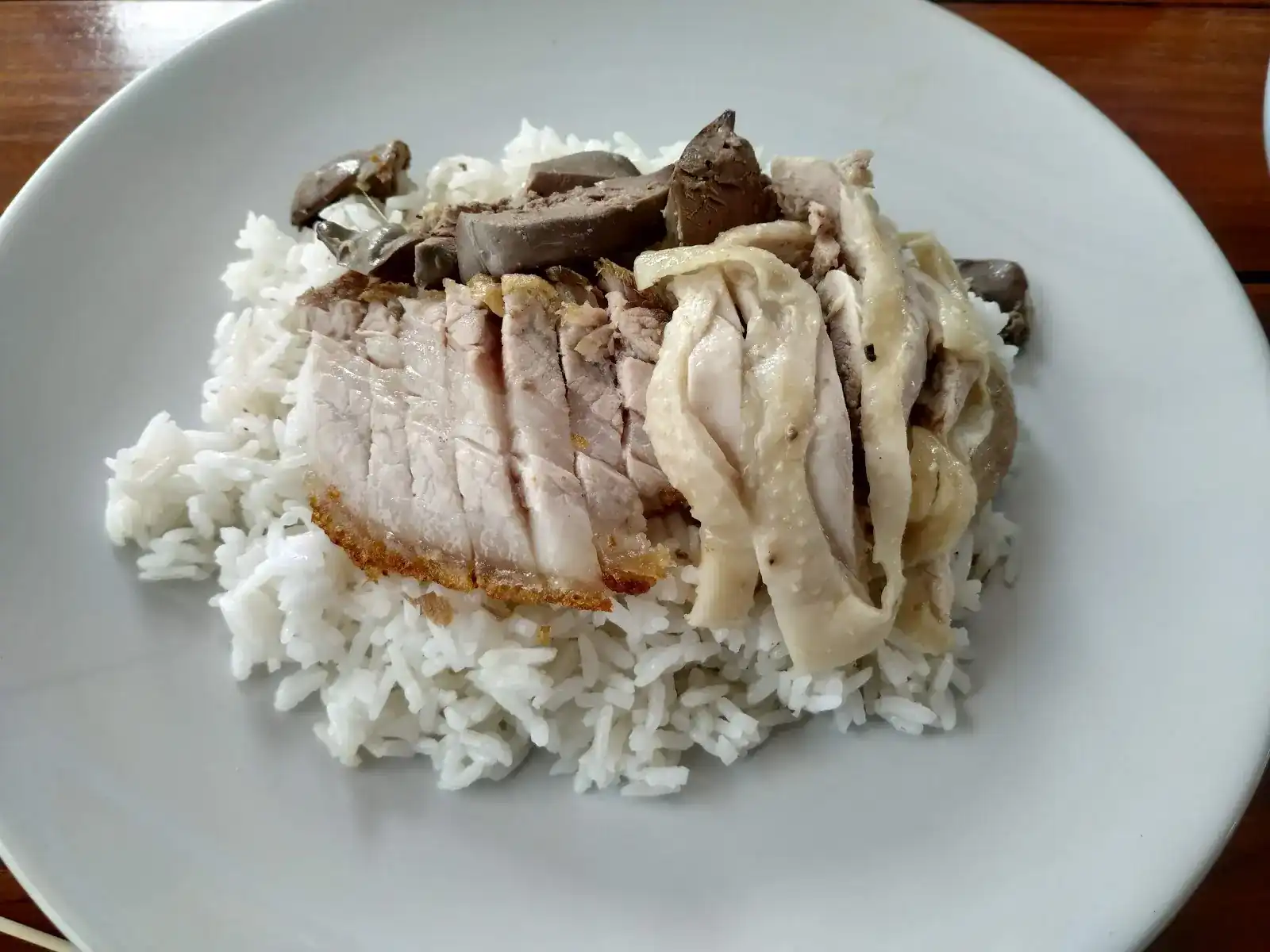 Chicken rice with sliced poached chicken, crispy pork and liver on a white plate